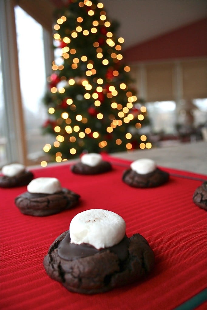 Hot chocolate cookies topped with marshmallows in front of a Christmas tree.