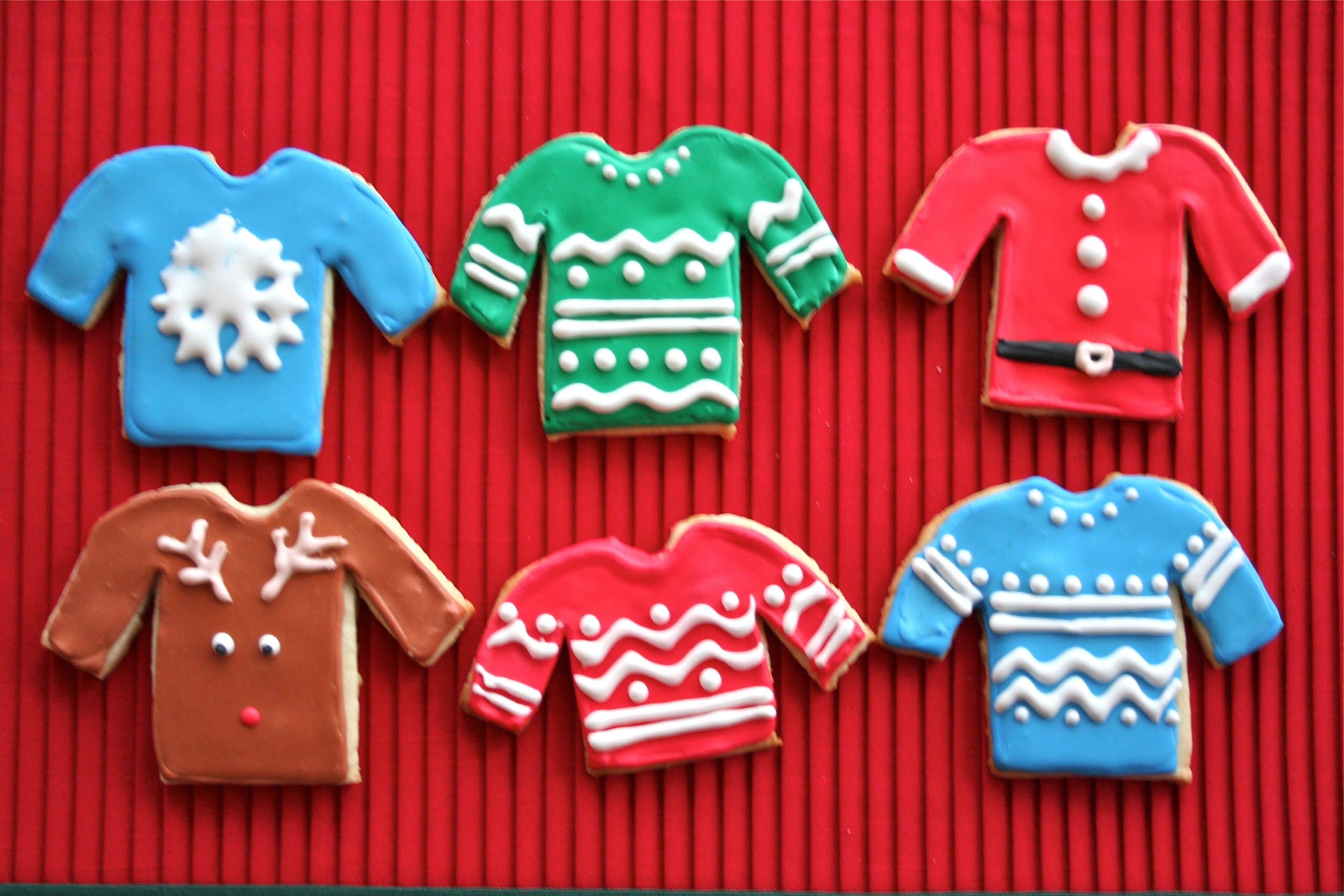 Six ugly sweater shaped cookies on a red placemat.