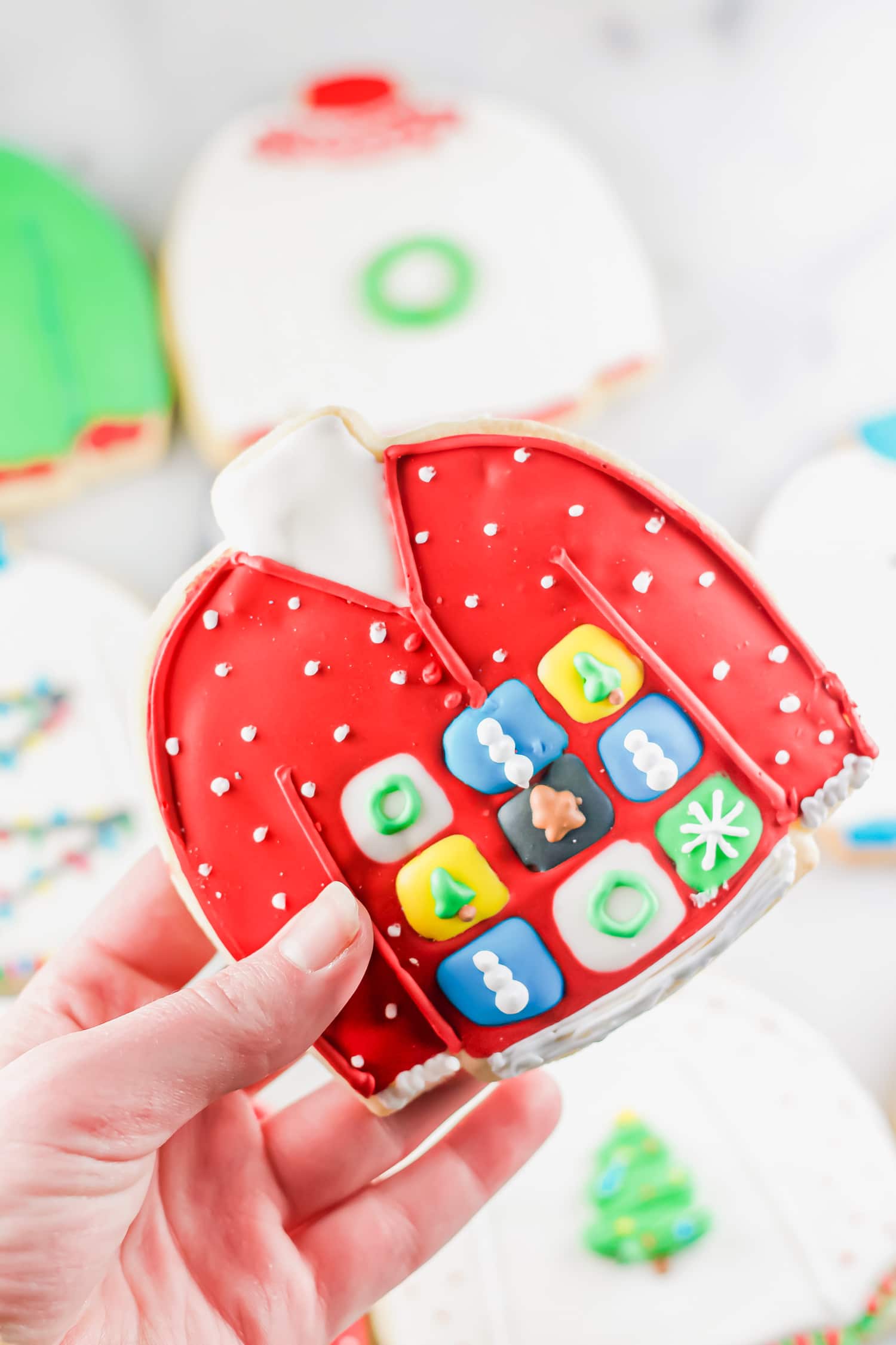 A photo of a hand holding a gluten-free ugly sweater cookie.