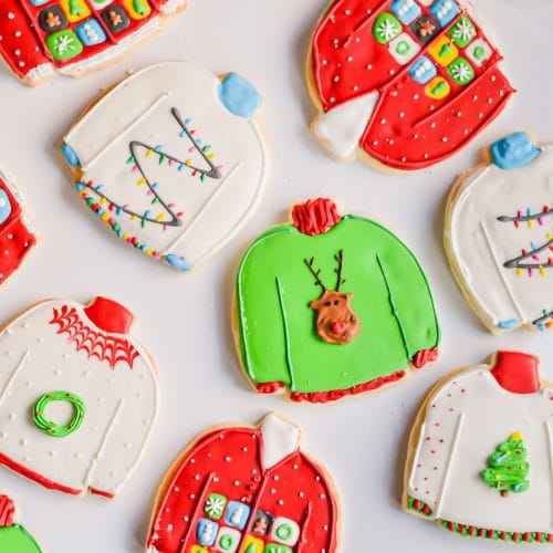 An overhead photo of decorated gluten-free ugly sweater sugar cookies on a white surface.