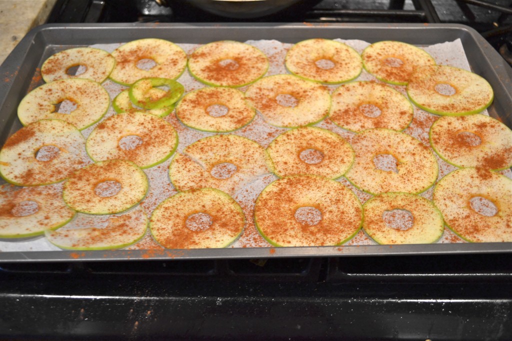 Thinly sliced apples sprinkled with ground cinnamon on a baking sheet.