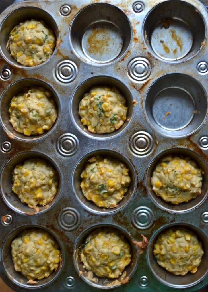 A muffin tin filled with baked corn fritters.