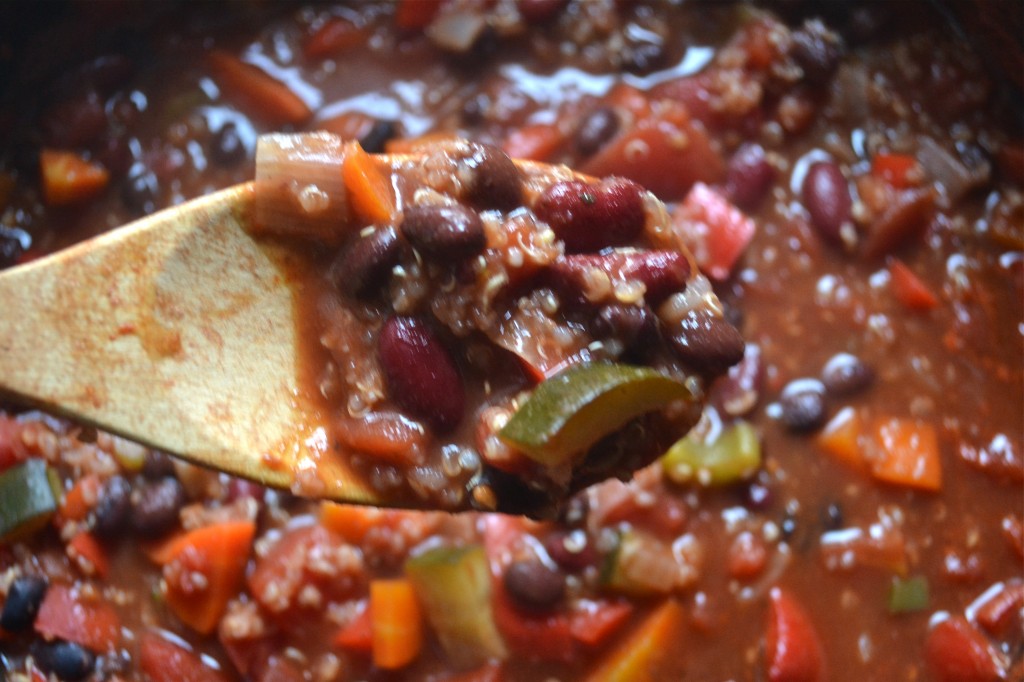 A wooden spoon full of vegetable quinoa chili over a large saucepan of chili.