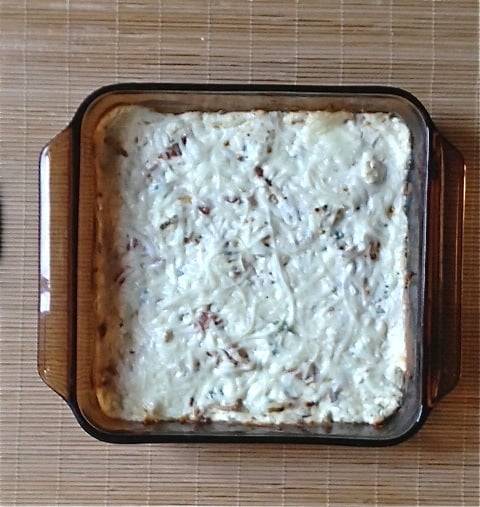 A casserole dish of warm bleu cheese bacon dip on a bamboo placemat.