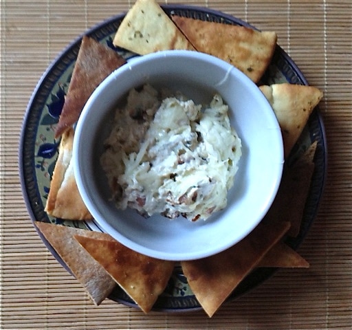 A bowl of bleu cheese bacon dip surrounded by gluten-free pita chip wedges.