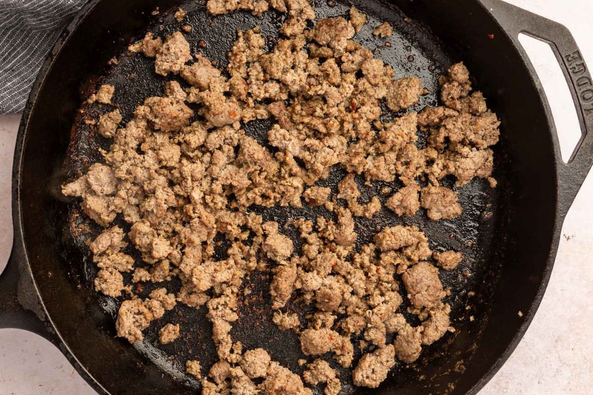 Breakfast sausage crumbles browning in a cast iron skillet