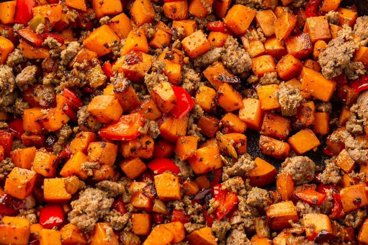 Close-up of sausage sweet potato hash with bell peppers in a cast iron skillet.