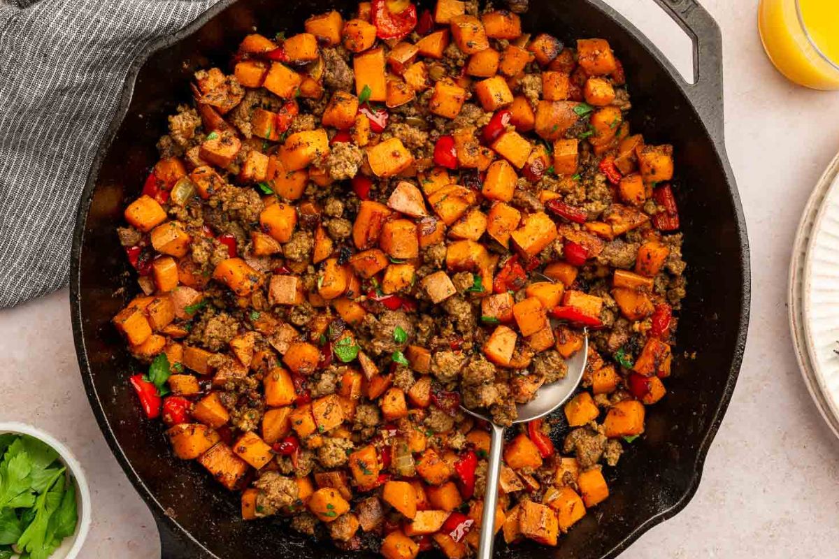 Finished sausage sweet potato hash in a cast iron skillet with a serving spoon.