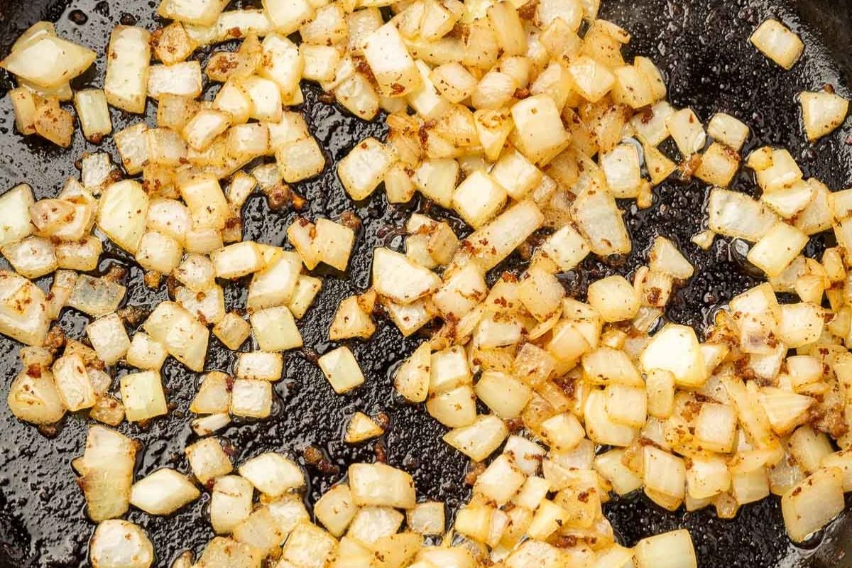 Diced onions sautéing in a cast iron skillet until golden and translucent.