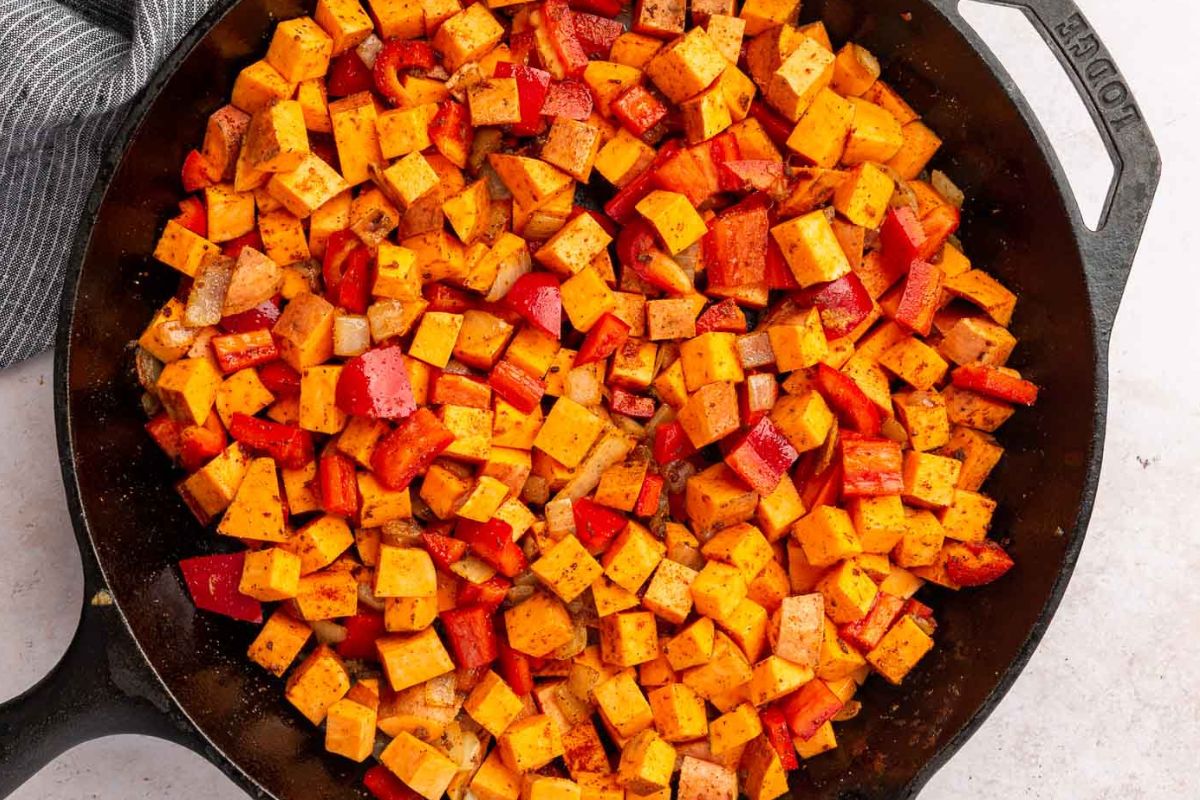 Sweet potatoes and bell peppers tossed with spices in a cast iron skillet.