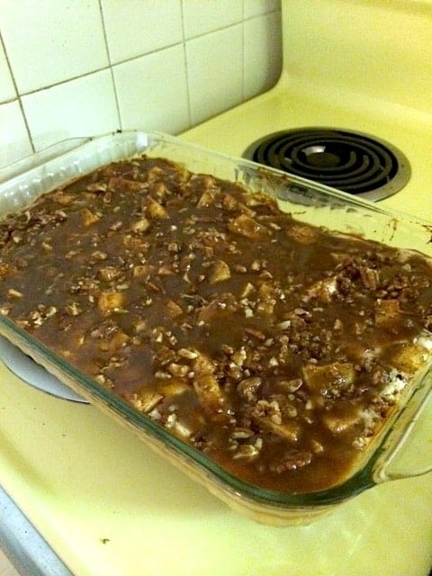 A casserole dish of caramel apple cheesecake bars topped with pecans.