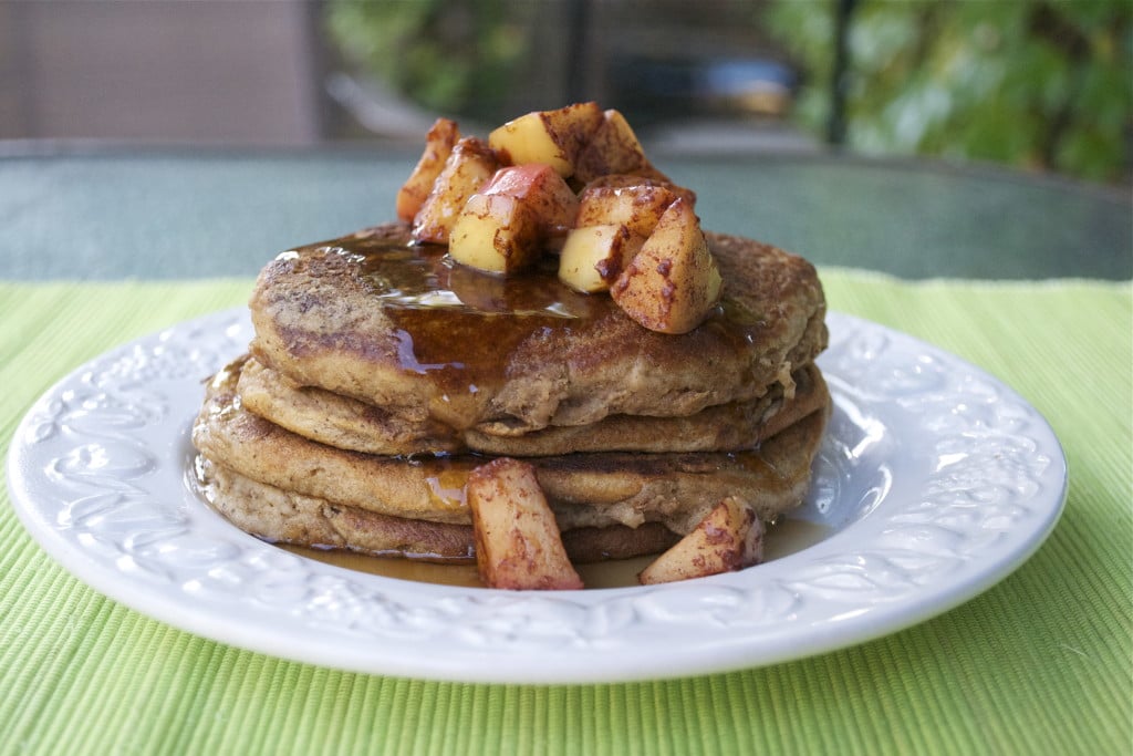 A stack of apple cider pancakes topped with sautéed apples and maple syrup on a white plate.
