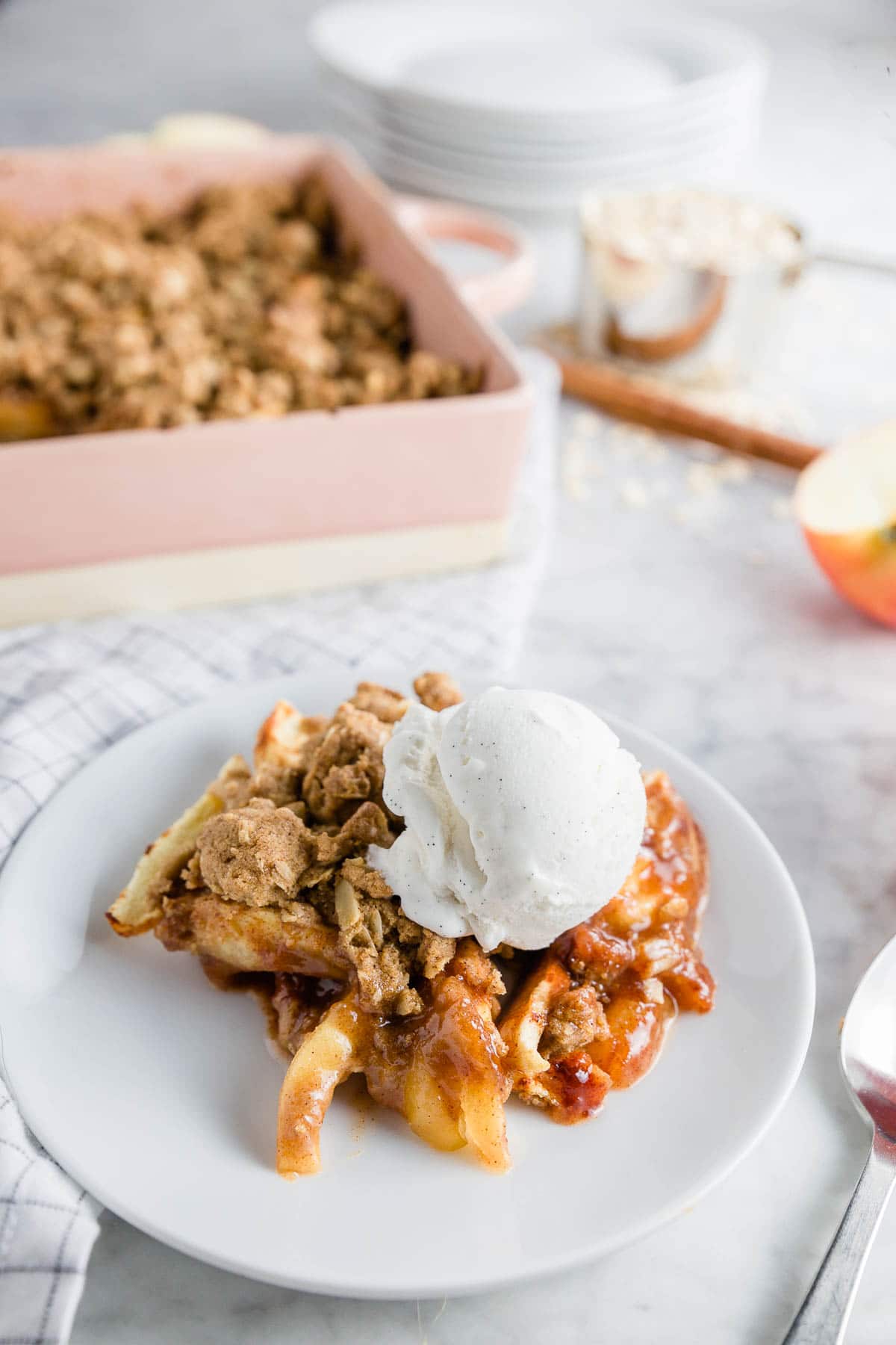 A plate with gluten-free apple crisp with a scoop of vanilla ice cream and a baking dish with apple crisp ready for serving. 