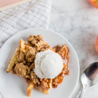 A white plate with gluten-free apple crisp and a scoop of vanilla bean ice cream.