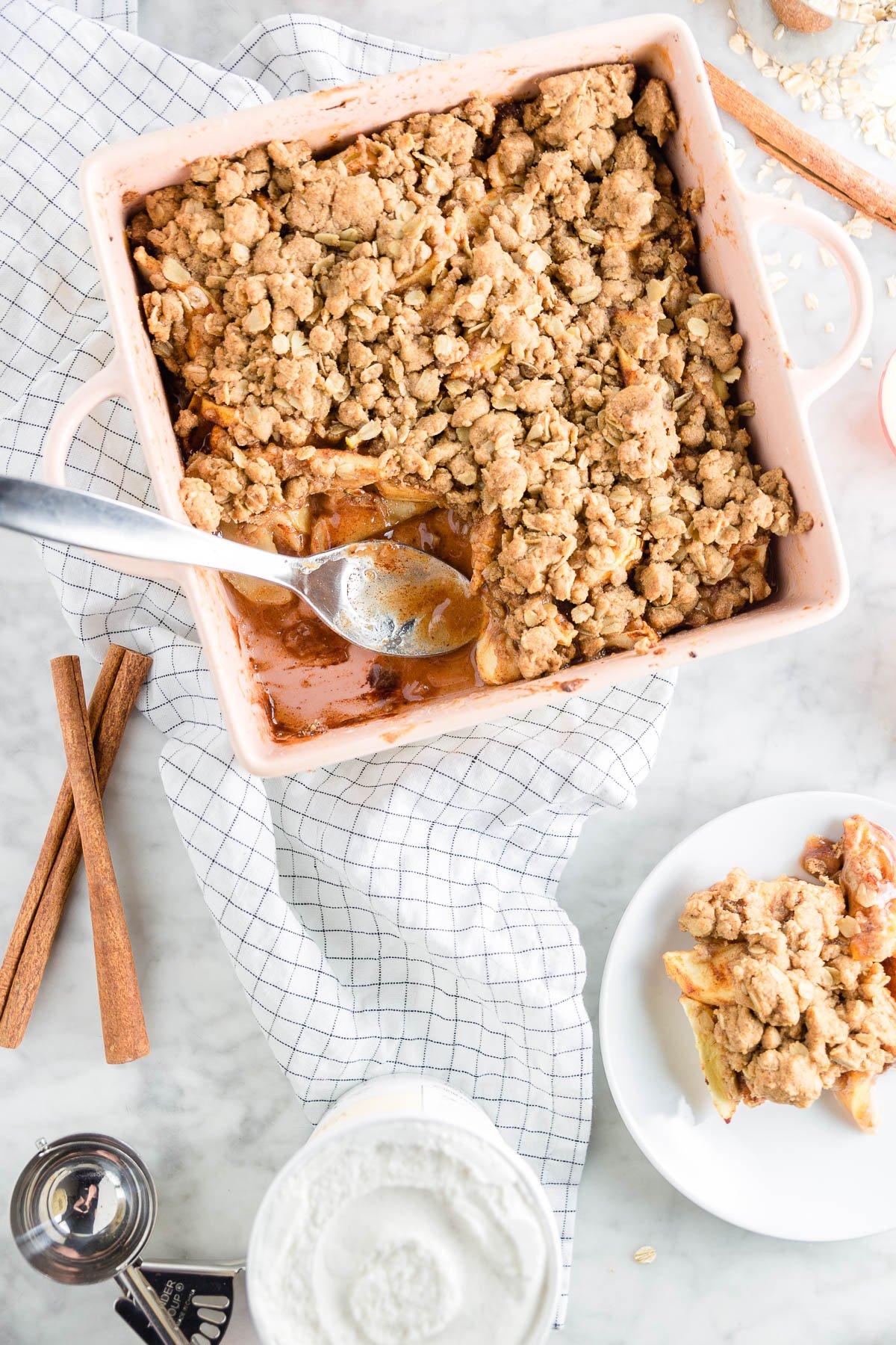 A square baking dish with gluten-free apple crisp and a plate with a big scoop. 