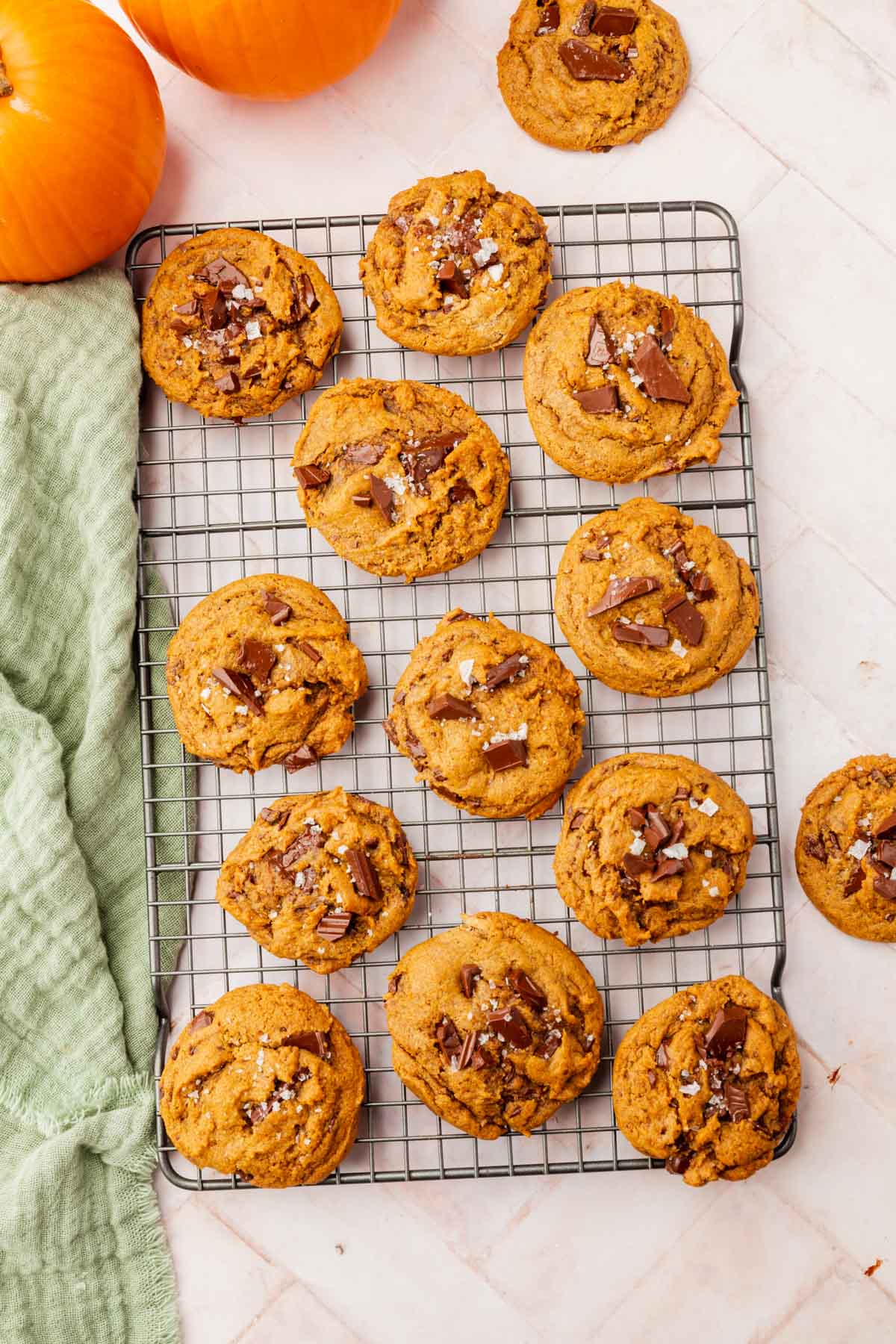 An overhead view of a cooling rack filled with gluten-free pumpkin chocolate chunk cookies with sea salt next to a green linen napkin.