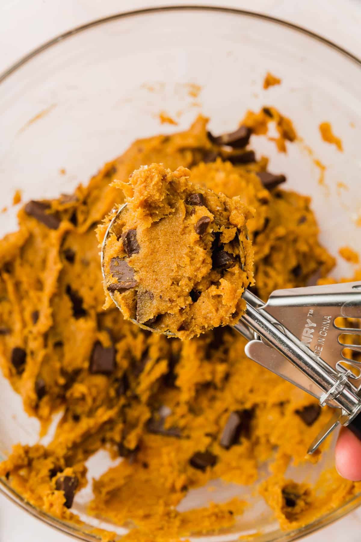 A portion scoop filled with gluten-free pumpkin chocolate chip cookie dough over a bowl of cookie dough.