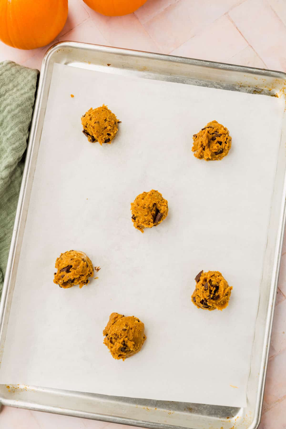 Six balls of gluten-free pumpkin chocolate chip cookie dough on a parchment lined baking sheet.