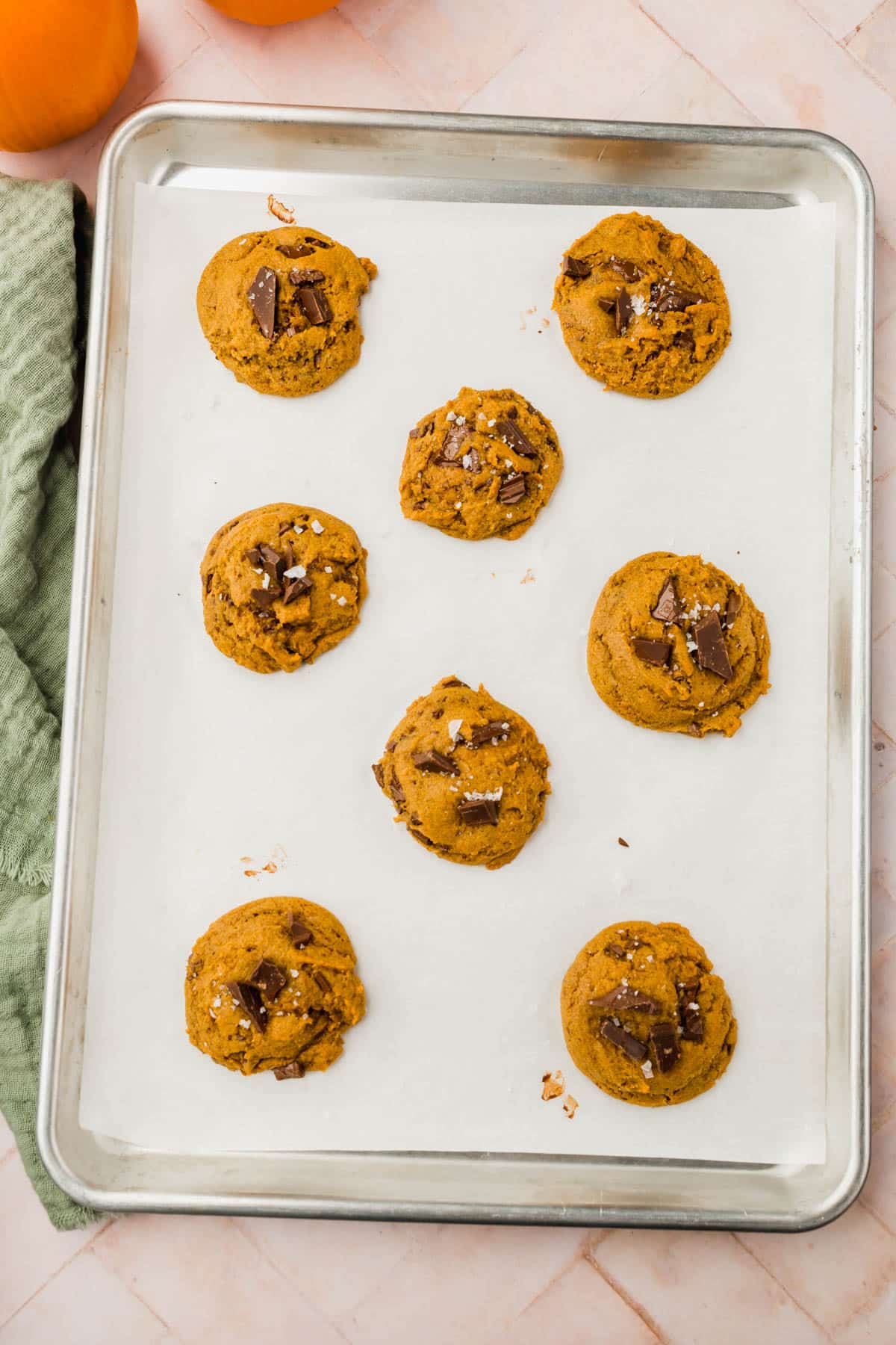 A baking sheet lined with parchment paper with gluten-free pumpkin chocolate chip cookies staggered on the baking sheet.