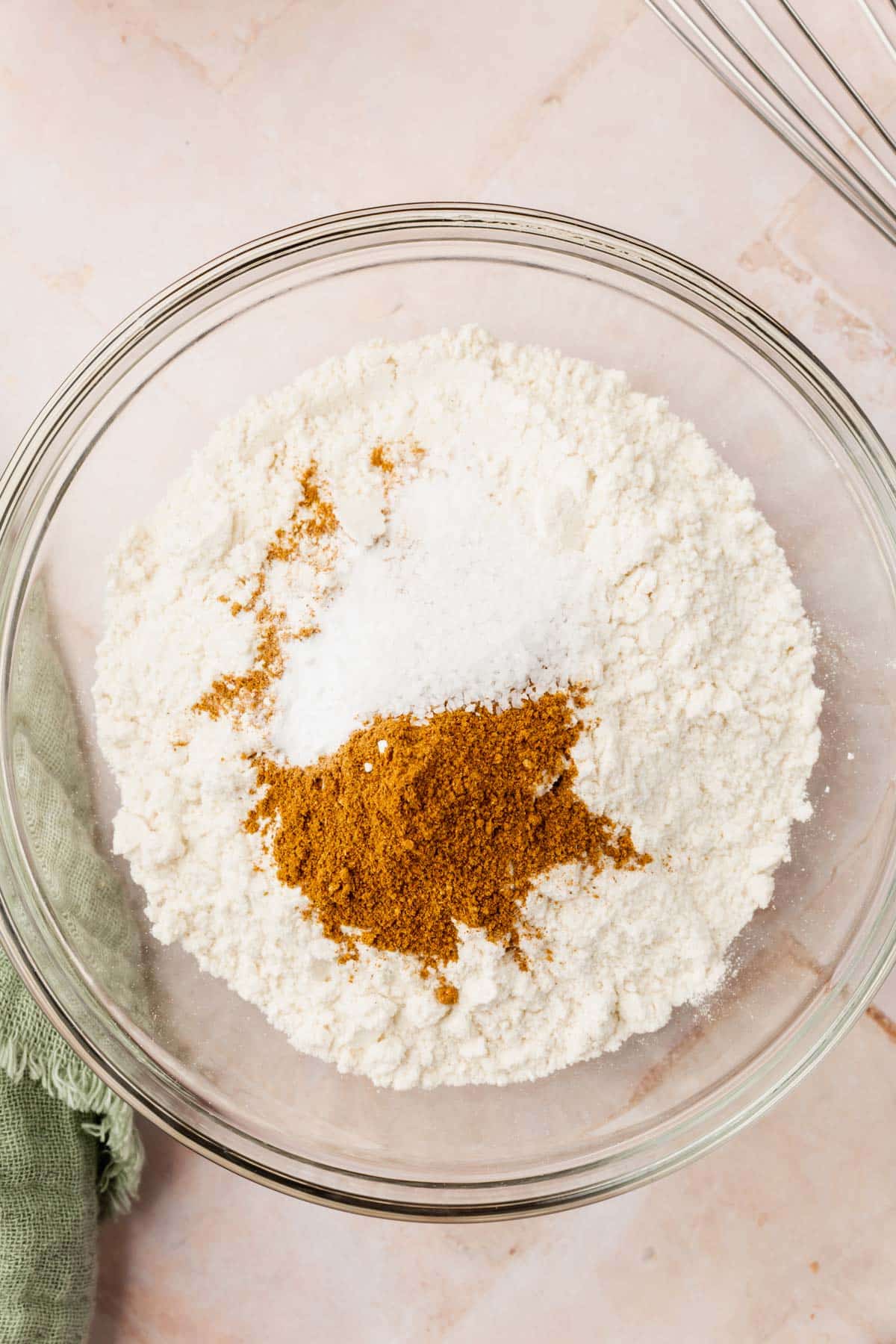 A glass mixing bowl with gluten-free flour, baking soda, baking powder, and pumpkin spice in it before mixing together.