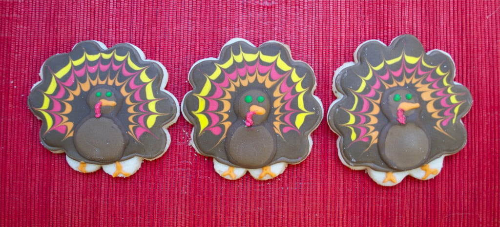 Three gluten-free turkey decorated sugar cookies on a red placemat.