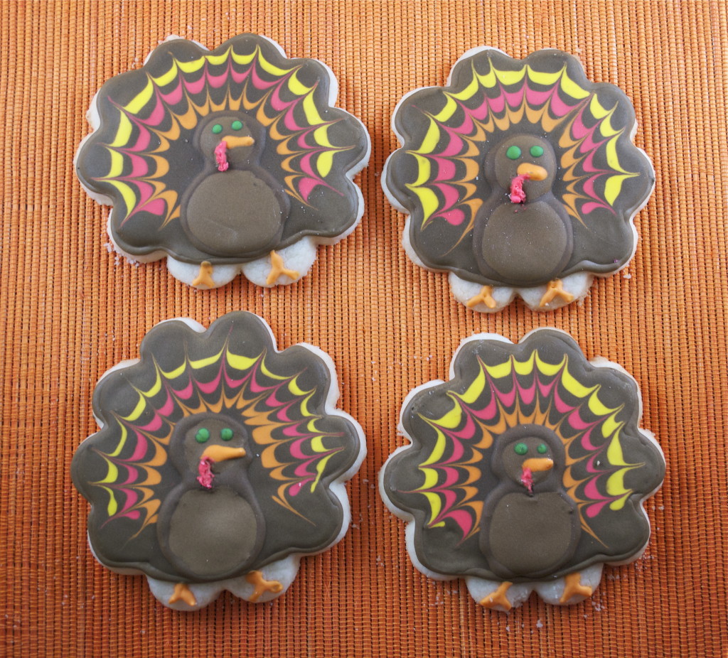 Four gluten-free sugar cookies decorated like turkeys on an orange placemat.