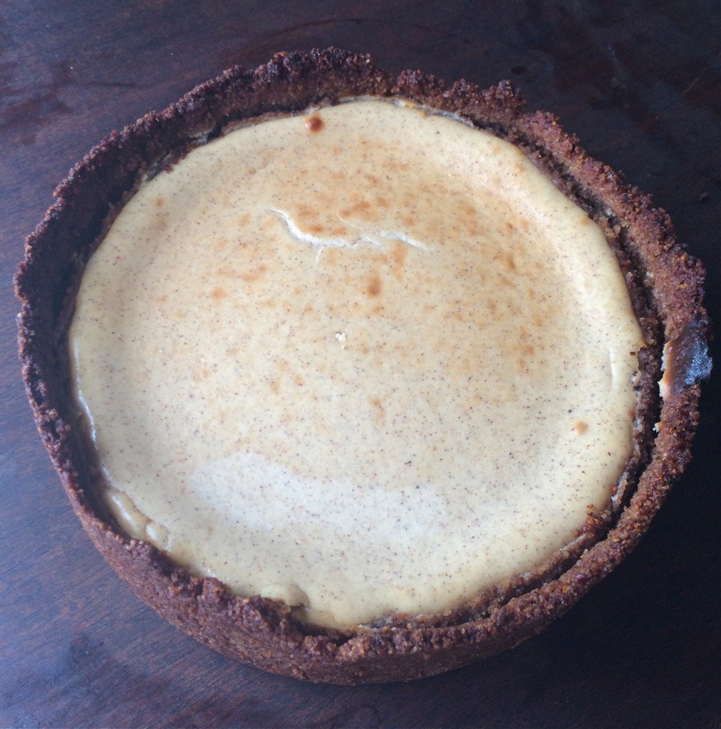 A pumpkin spice cheesecake with pecan crust on a table.