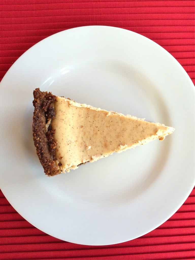 A slice of pumpkin pie cheesecake with pecan crust on a white plate.