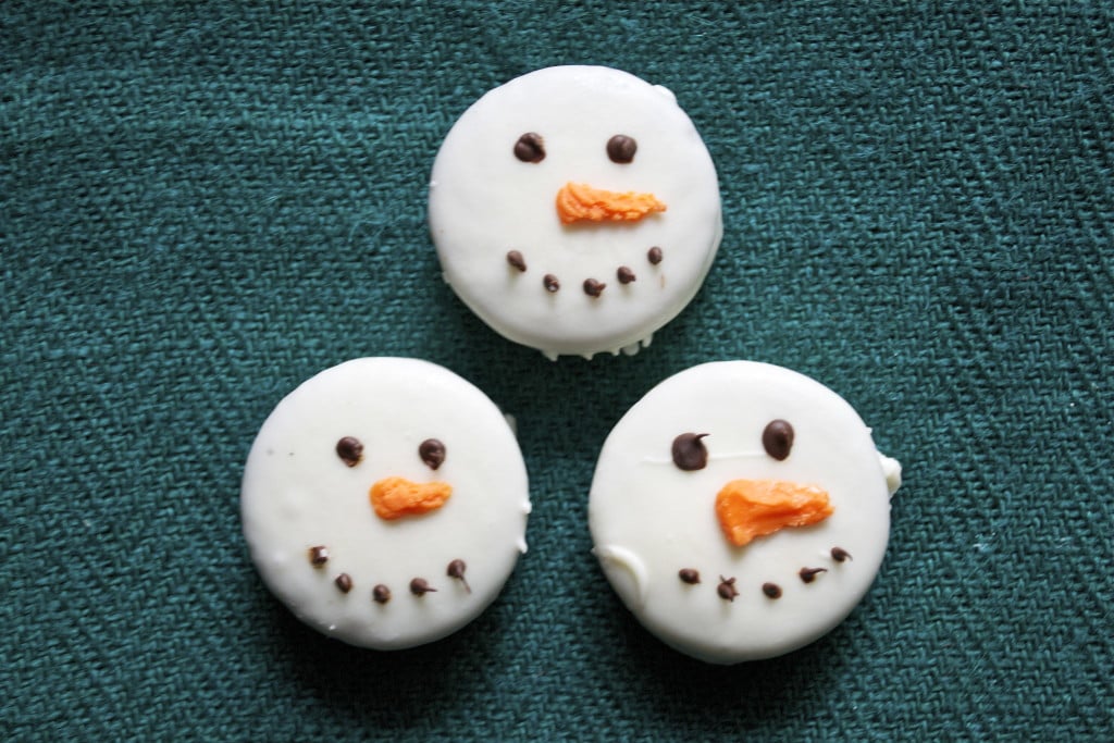 White chocolate dipped Oreo Snowmen on a green placemat.