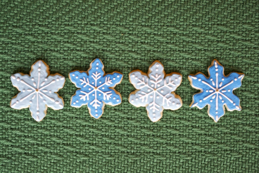 Four Snowflake decorated Sugar Cookies on a green placemat.