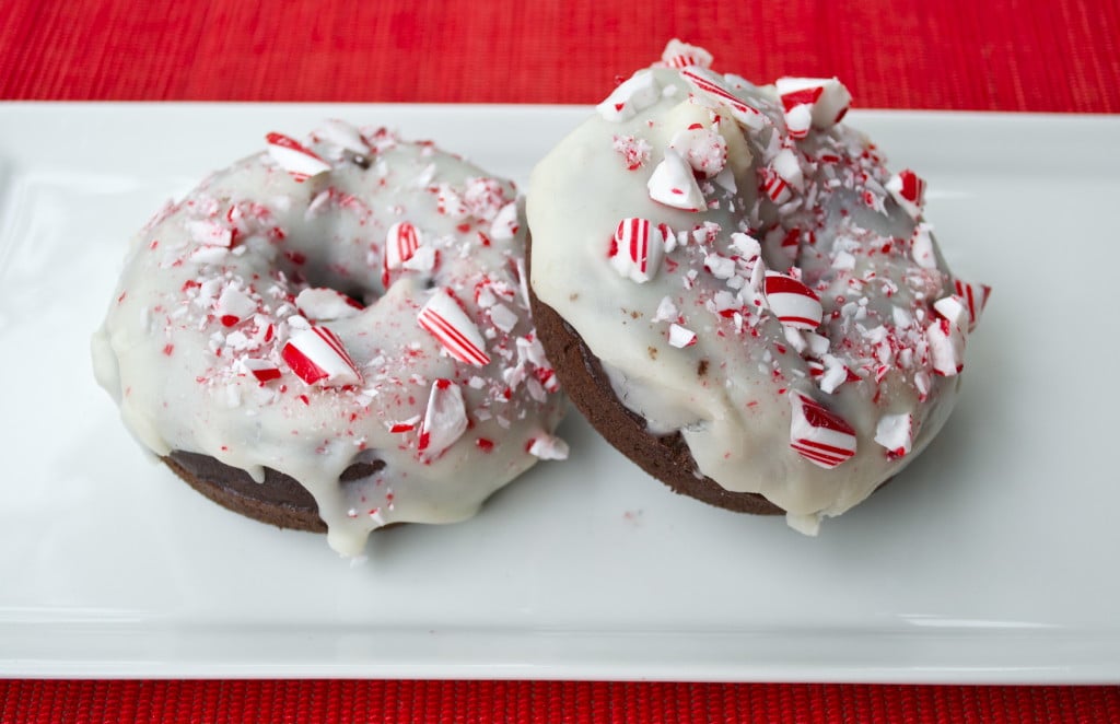 Two chocolate donuts topped with white chocolate and crushed candy canes.