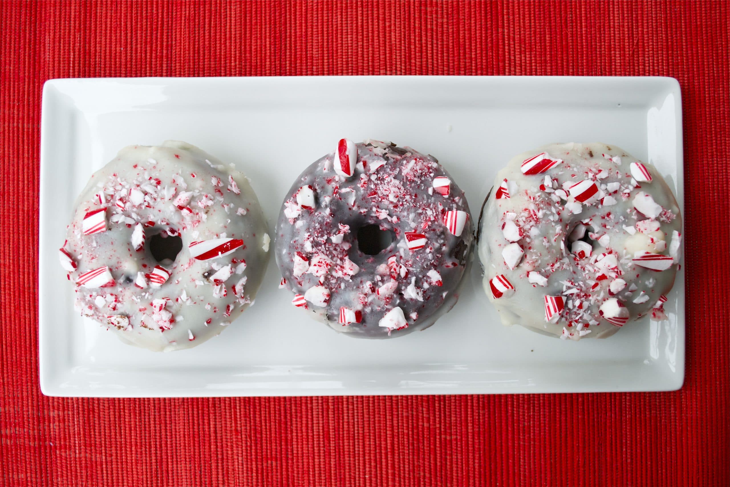 A platter with three Gluten-Free Chocolate Peppermint Donuts topped with crushed candy canes.