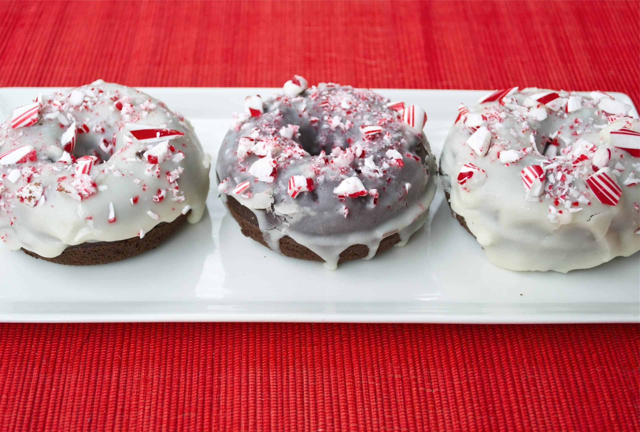 A plate of three chocolate donuts topped with white chocolate glaze and crushed candy canes.