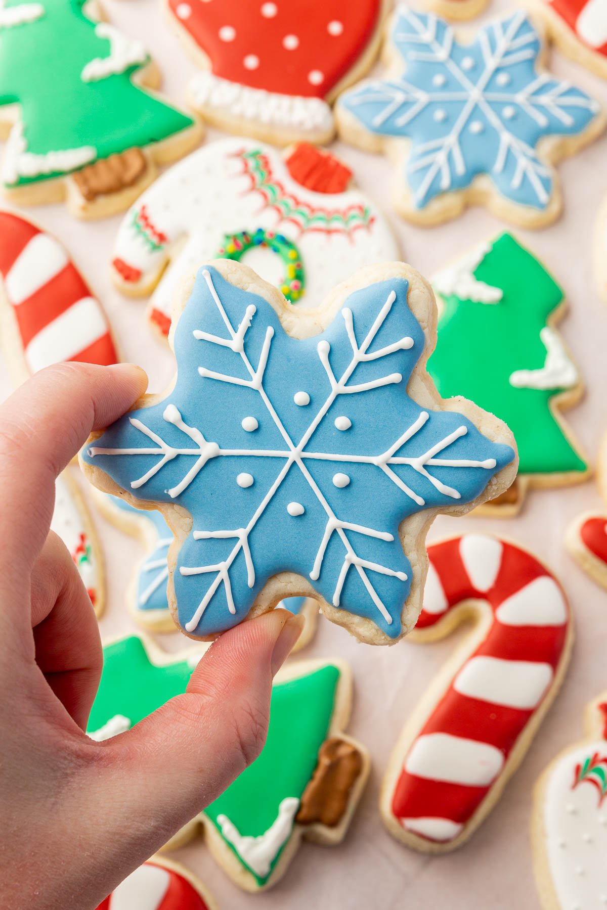 A hand holding a snowflake sugar cookie over a pan of gluten-free Christmas sugar cookies. 