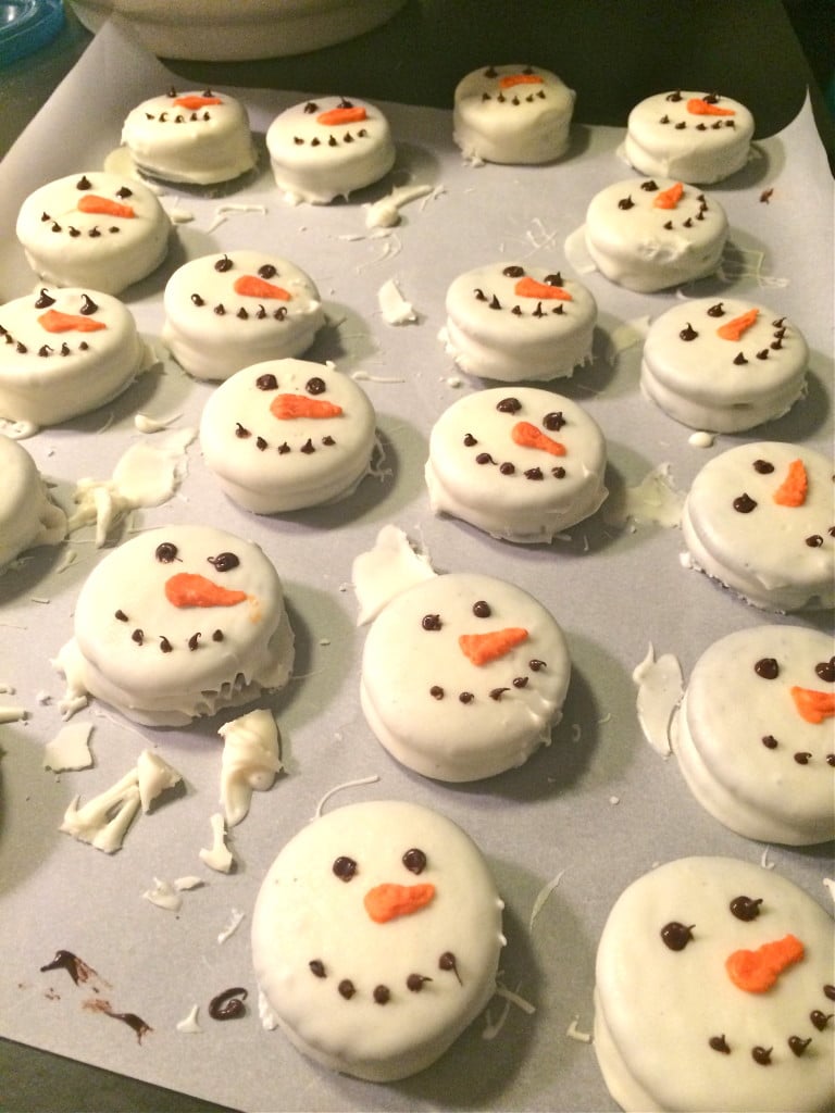 Chocolate dipped oreos decorated like snowman faces on a piece of parchment paper.