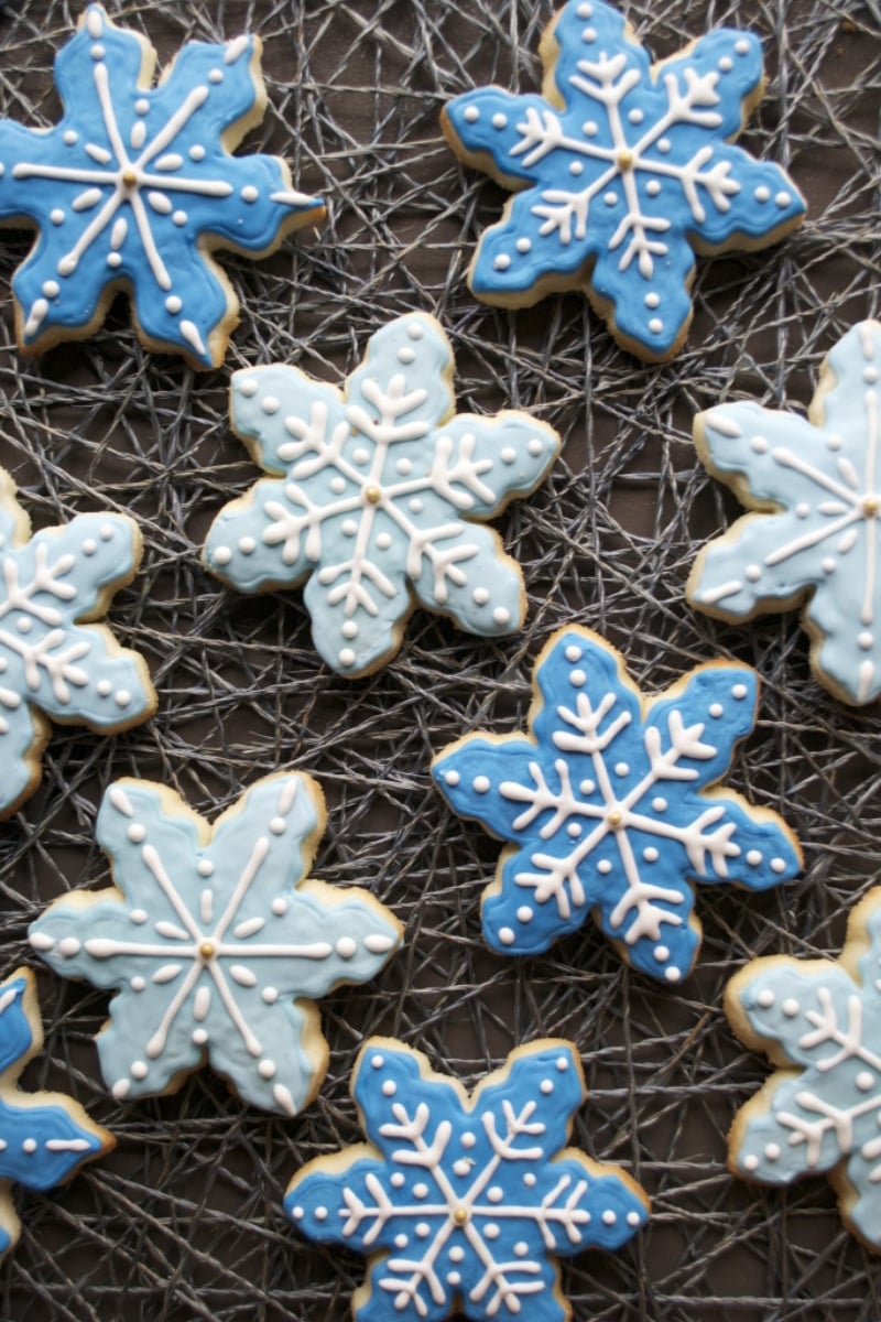 Multiple snowflake sugar cookies decorated with blue and white royal icing on a webbed place mat. 