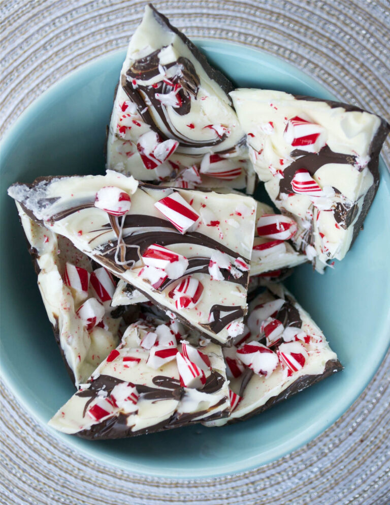 Homemade chocolate peppermint bark with red and white candy cane pieces and chocolate swirls in a teal bowl.