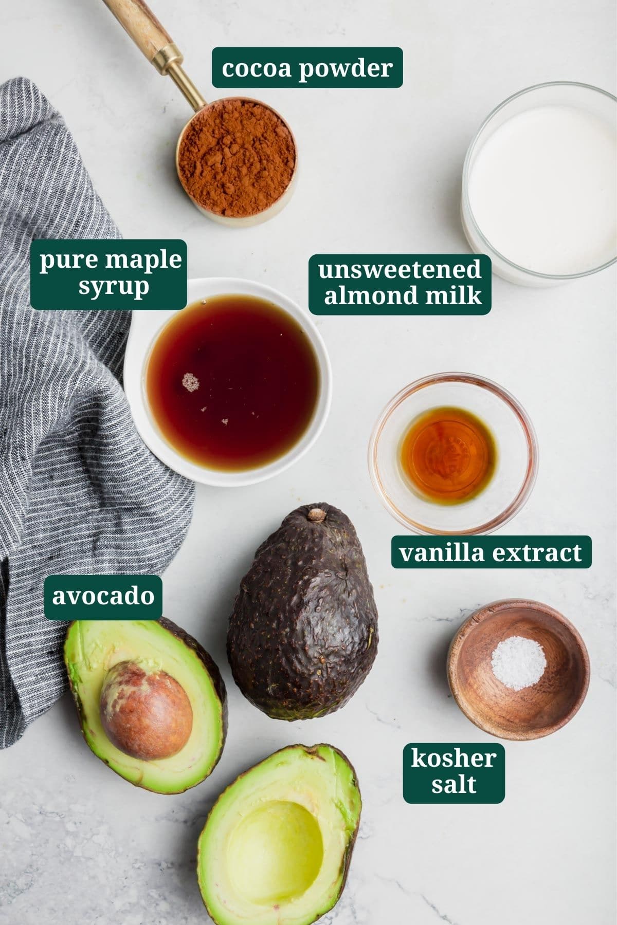 Ingredients for avocado chocolate pudding on a table - maple syrup, salt, vanilla, cocoa powder, almond milk, avocado.