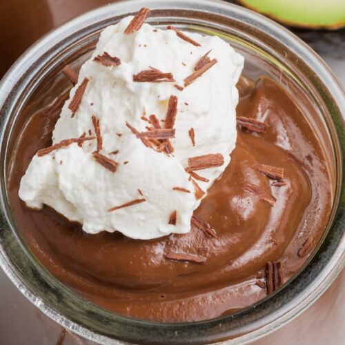A glass jar filled with creamy chocolate avocado pudding, topped with a dollop of whipped cream and chocolate shavings.