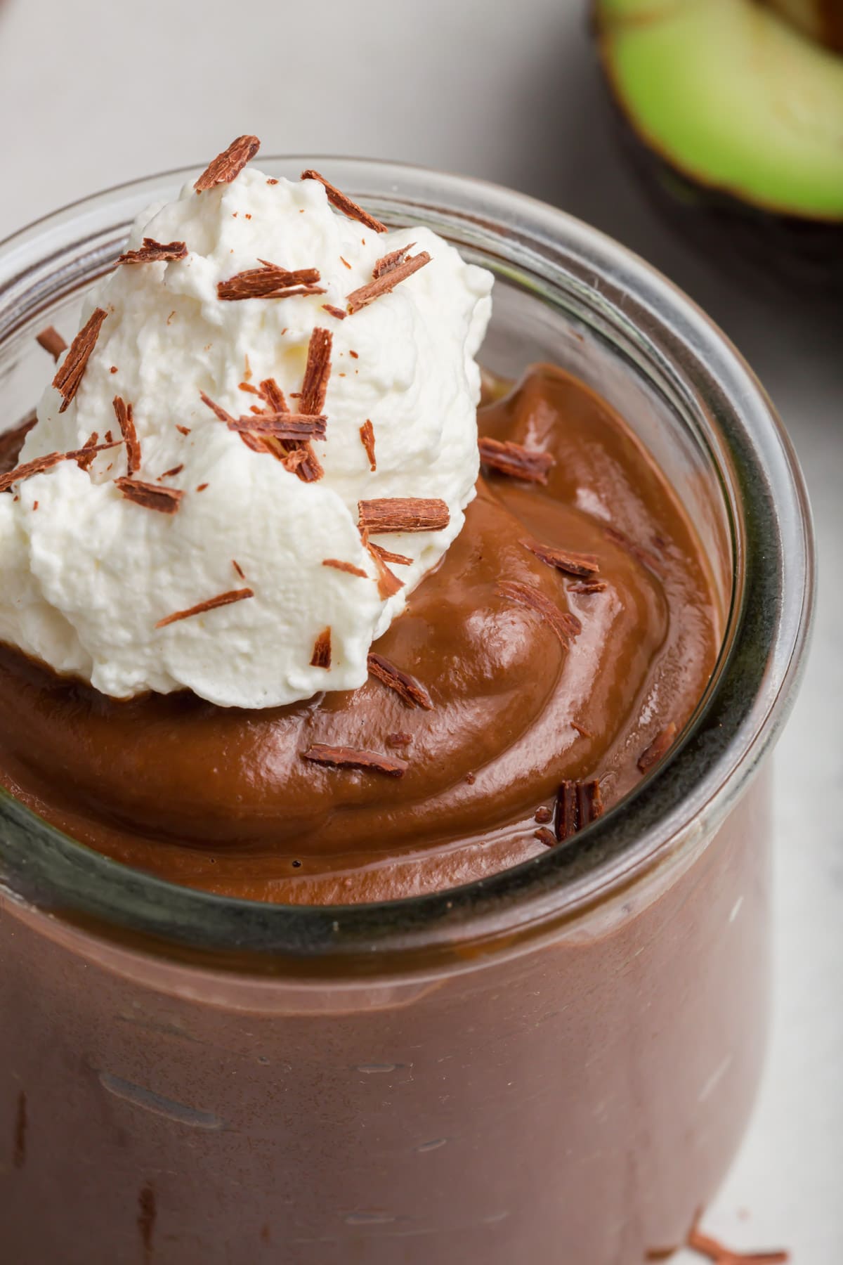 A jar of avocado chocolate pudding with coconut whipped cream and chocolate shavings. 