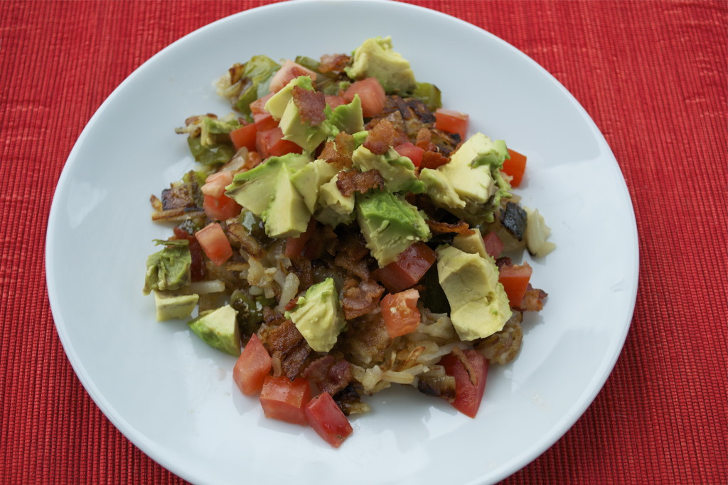 A plate of hash browns topped with bacon, diced avocado, tomatoes, and bell peppers.