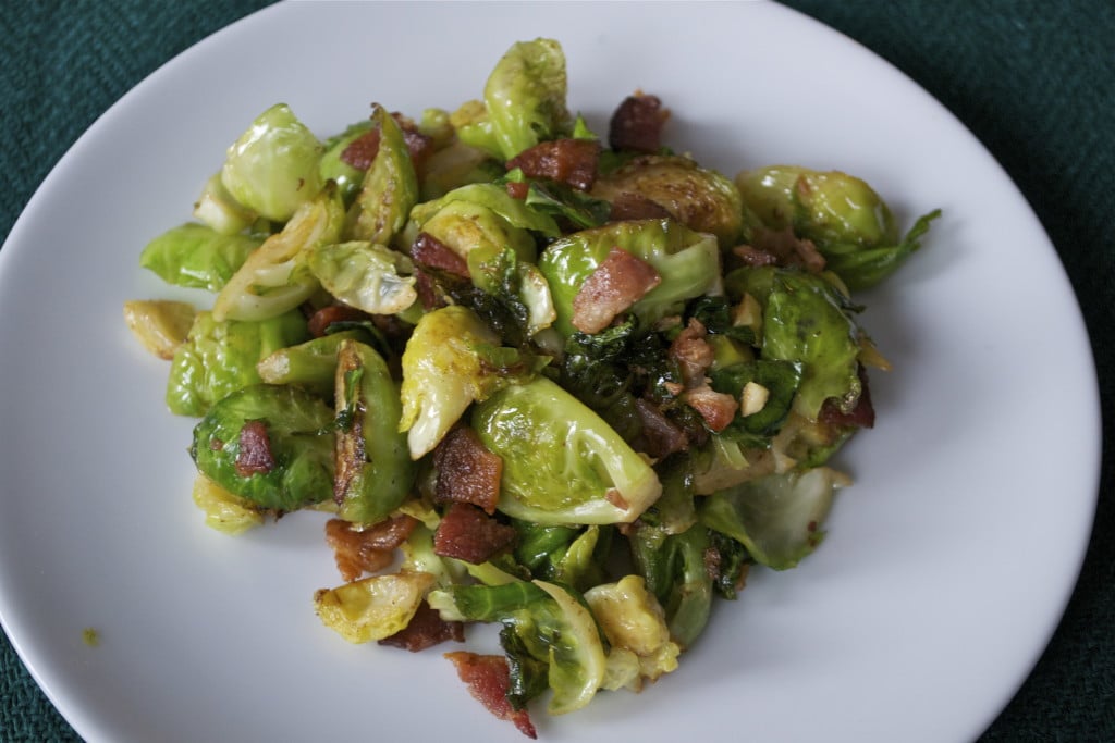 A plate of sautéd brussels sprouts topped with bacon. 