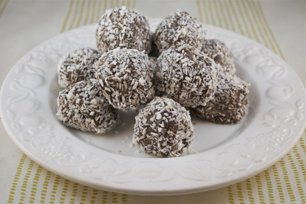Chocolate coconut balls rolled in shredded coconut on a white plate.