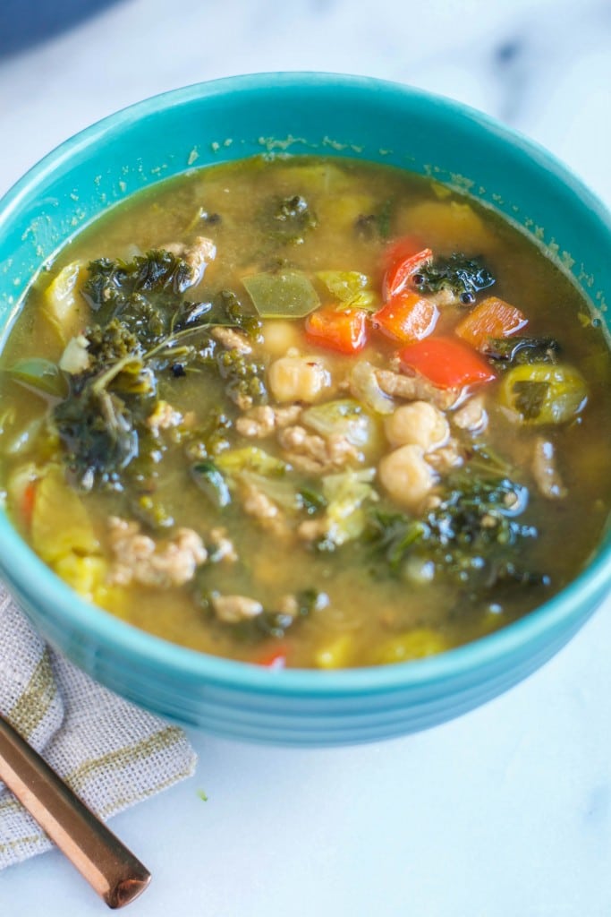 A bowl of turkey soup with kale, chickpeas, brussels sprouts and bell peppers. 