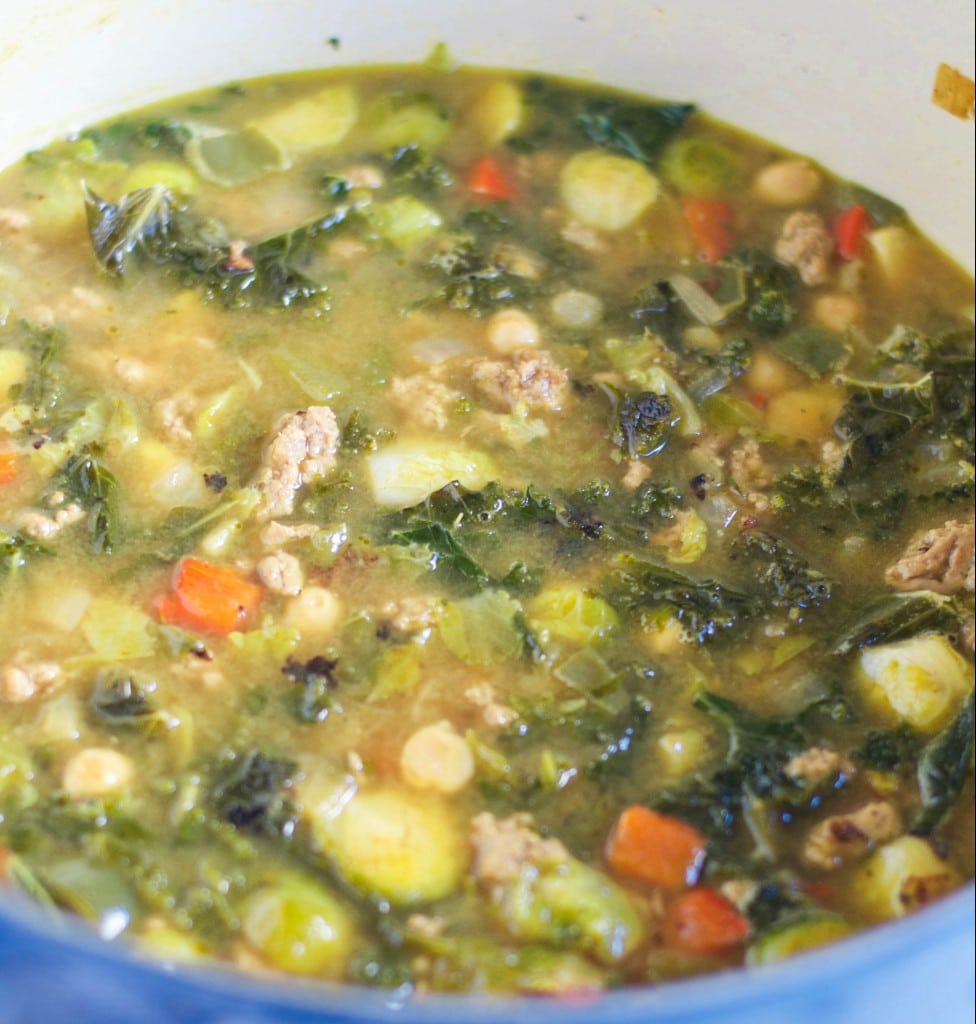 A stock pot of turkey soup with kale, chickpeas, and brussels sprouts in a vegetable broth. 