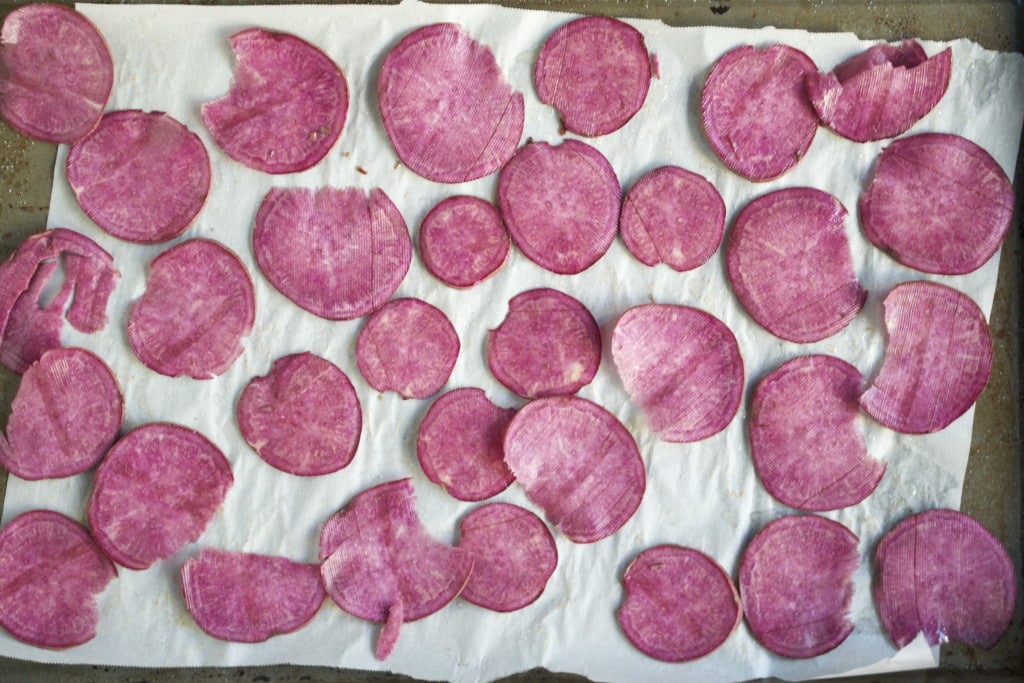 Thinly sliced purple sweet potatoes on a baking sheet lined with parchment paper.