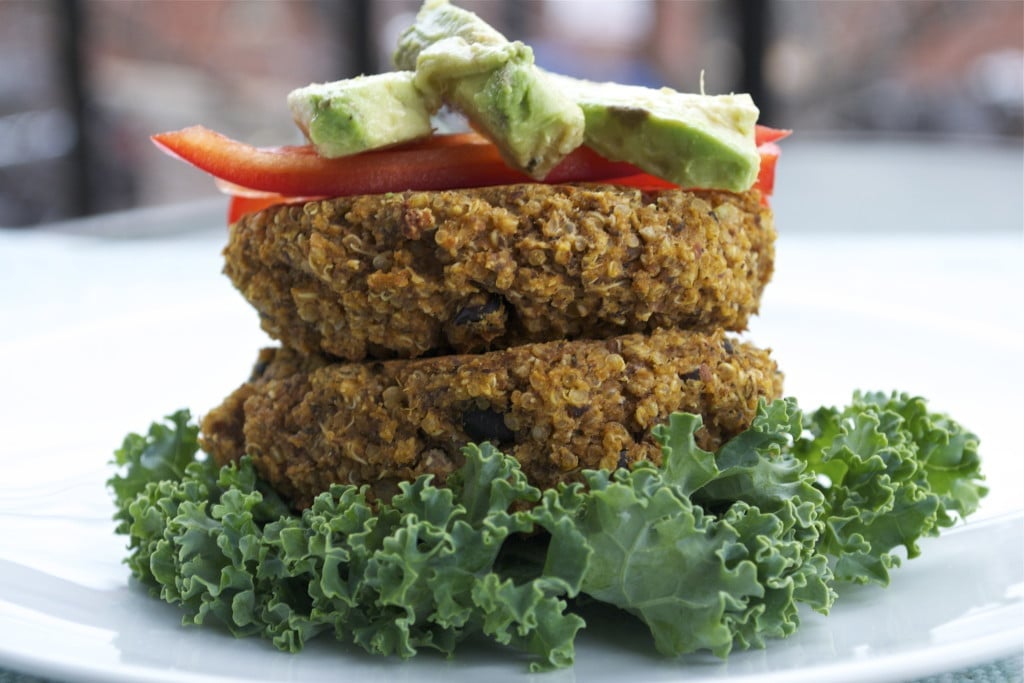 A stack of two sweet potato quinoa burgers on curly lettuce topped with red bell peppers and sliced avocado. 