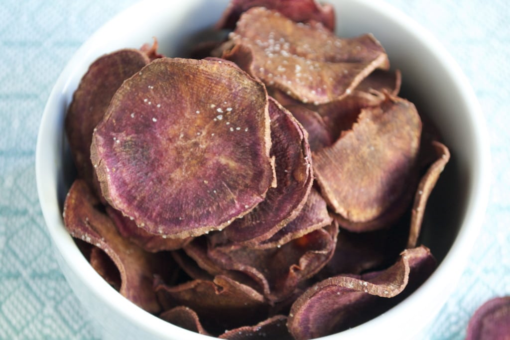 Baked purple sweet potato chips topped with salt in a white ramekin.