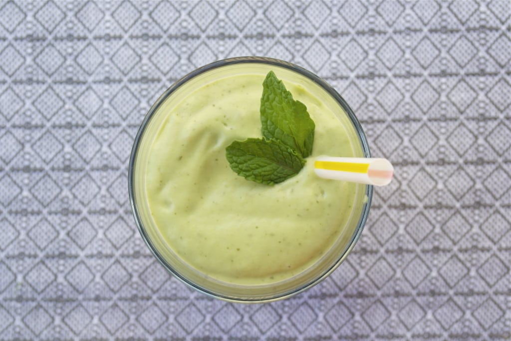 An overhead view of a healthy shamrock shake topped with fresh mint leaves and a straw.