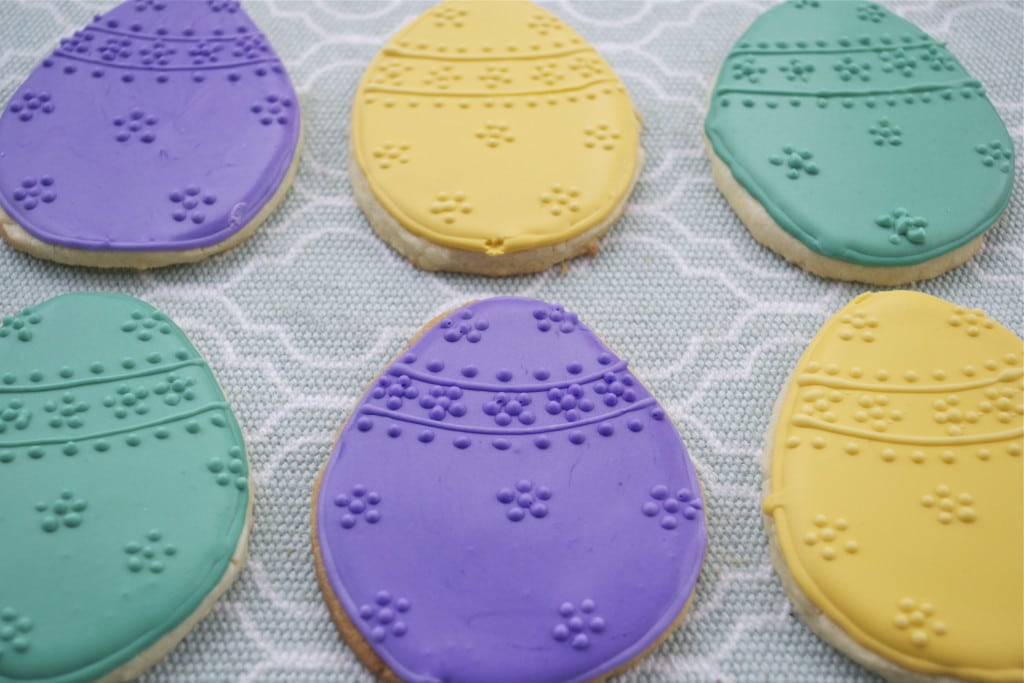 Sugar cookies decorated with purple, yellow and green royal icing to look like Eggs with raised dot designs.